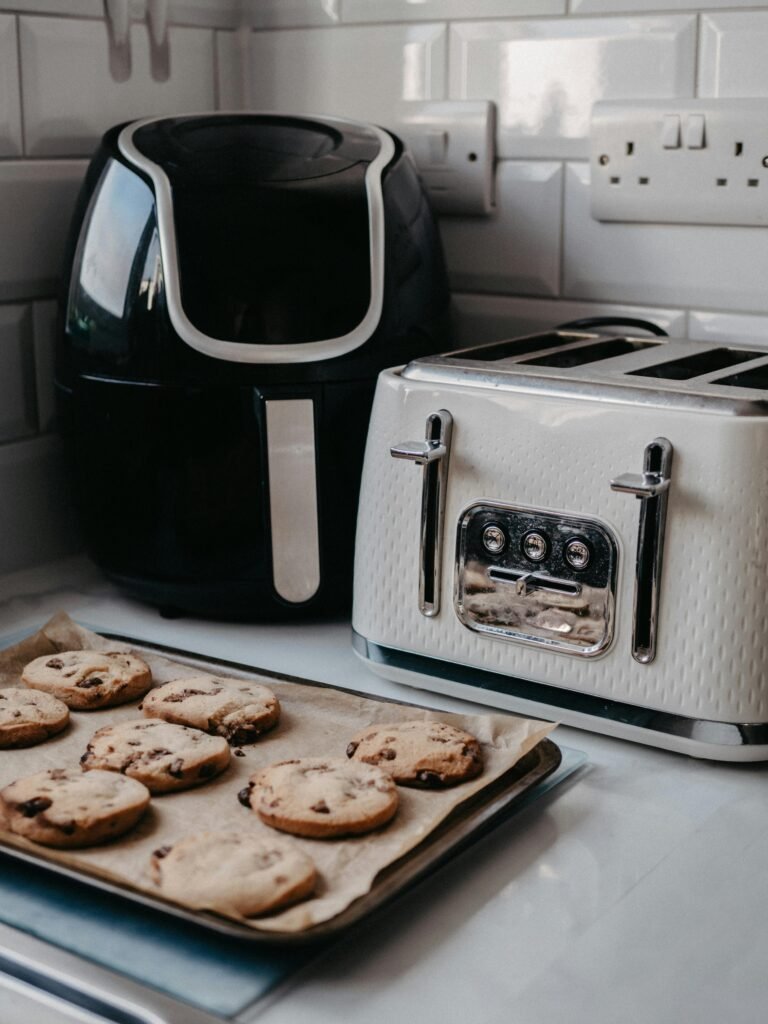 Freshly baked cookies on tray beside air fryer and toaster.